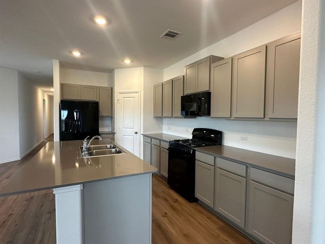 Kitchen featuring black appliances, a sink, gray cabinets, dark wood-style flooring, and a kitchen island with sink | Image 20