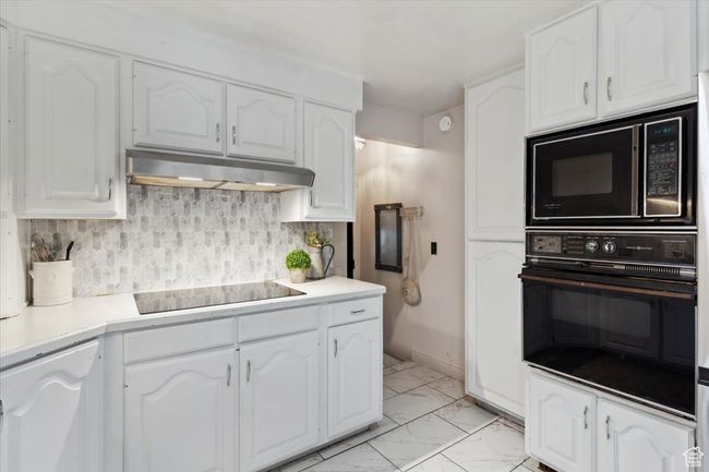 Kitchen with black appliances, under cabinet range hood, light marble finish flooring, and white cabinetry | Image 10
