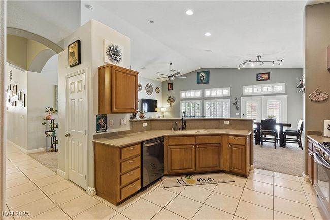 Kitchen featuring brown cabinets, a sink, a peninsula, black dishwasher, and ceiling fan | Image 7