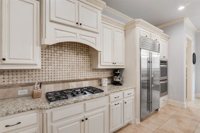 Kitchen with appliances with stainless steel finishes, backsplash, light tile patterned floors, ornamental molding, and light stone counters | Image 5