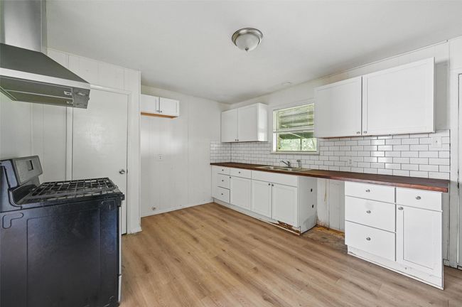 Kitchen featuring wood counters, black gas range, wall chimney exhaust hood, a sink, and light wood-style floors | Image 13