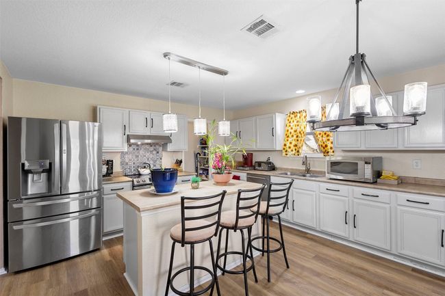 Kitchen with a sink, wood finished floors, appliances with stainless steel finishes, under cabinet range hood, and visible vents | Image 13