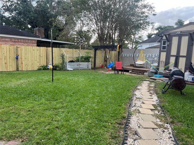 This backyard features a well-maintained lawn with a paved walkway. There's a wooden fence for privacy, a shed, and a patio area with seating. It includes a swing set and grill, making it ideal for family activities and outdoor entertaining. | Image 8