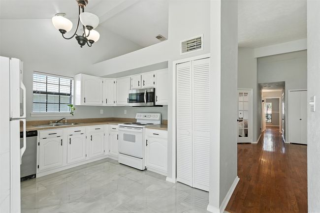 Kitchen featuring stainless steel appliances, high vaulted ceiling, a chandelier, healthy amount of natural light, and white cabinets | Image 10