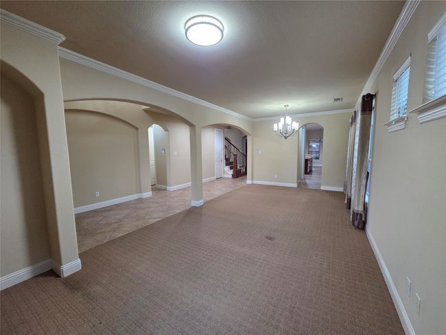 Spare room with light colored carpet, arched walkways, a chandelier, stairs, and crown molding | Image 7