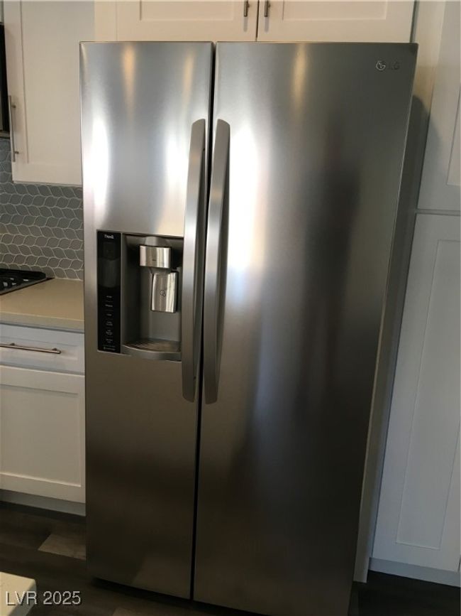 Room details with white cabinetry, tasteful backsplash, stainless steel fridge with ice dispenser, and light countertops | Image 11
