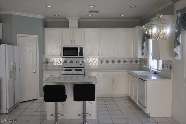 Kitchen with white appliances, a chandelier, light countertops, white cabinetry, and recessed lighting | Image 34