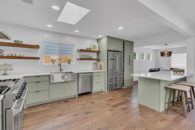 Kitchen with green cabinetry, open shelves, a sink, a kitchen breakfast bar, and high end appliances | Image 18