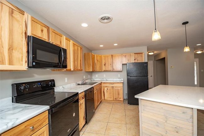 Kitchen with visible vents, decorative light fixtures, light tile patterned floors, black appliances, and a sink | Image 15