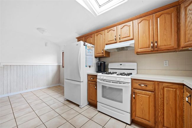 Kitchen with brown cabinetry, under cabinet range hood, white appliances, and a skylight | Image 5
