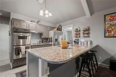 Kitchen with kitchen peninsula, gray cabinetry, stainless steel appliances, a notable chandelier, and decorative backsplash | Image 3