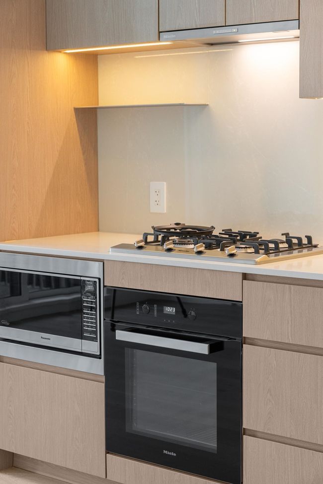 Kitchen with appliances with stainless steel finishes, light countertops, under cabinet range hood, light brown cabinetry, and modern cabinets | Image 17
