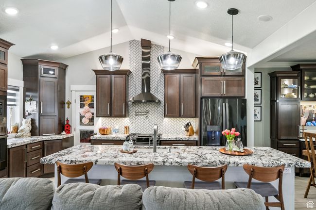 Kitchen with stainless steel fridge with ice dispenser, wall chimney exhaust hood, open floor plan, a breakfast bar area, and lofted ceiling | Image 26