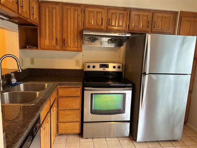 Kitchen with stainless steel appliances, ventilation hood, brown cabinetry, and light tile patterned flooring | Image 11