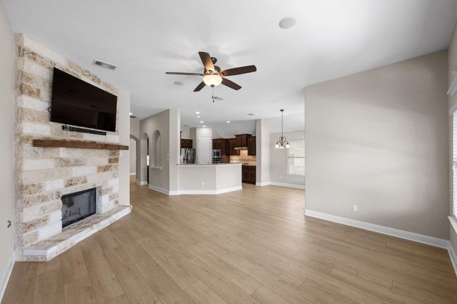 Unfurnished living room featuring ceiling fan, a stone fireplace, and light wood-style floors | Image 5