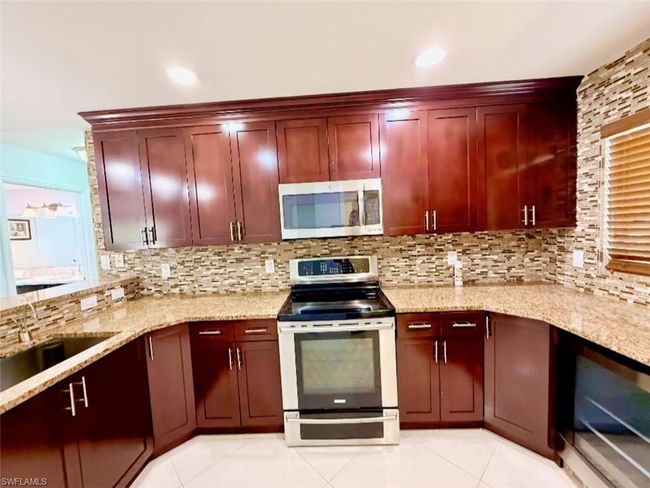 Kitchen with light tile patterned floors, decorative backsplash, a sink, appliances with stainless steel finishes, and reddish brown cabinets | Image 12