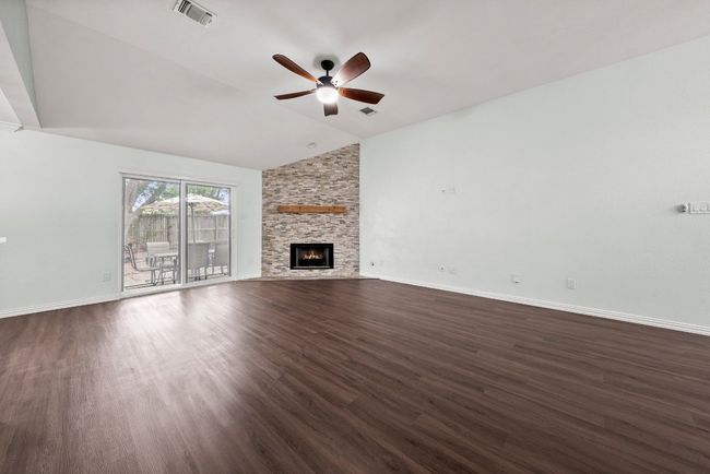 Unfurnished living room featuring a ceiling fan, lofted ceiling, dark wood-style flooring, a fireplace, and baseboards | Image 6