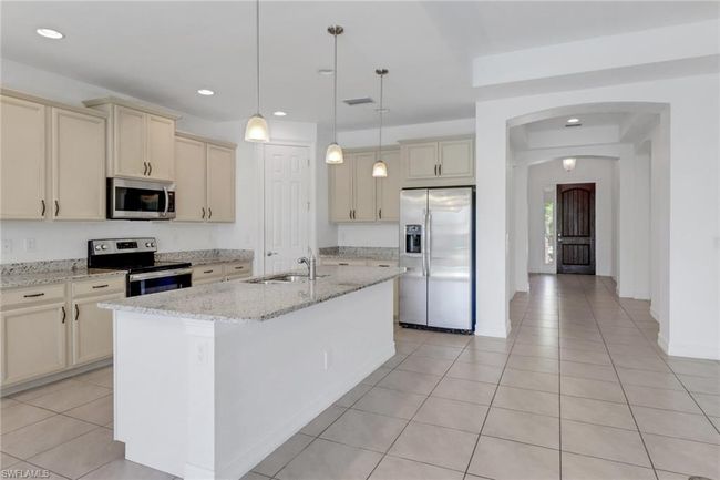 Kitchen featuring stainless steel appliances, a sink, cream cabinets, light tile patterned flooring, and a kitchen island with sink | Image 27