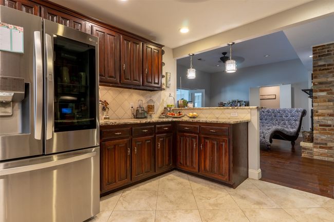Kitchen featuring stainless steel fridge with ice dispenser, backsplash, a peninsula, light stone countertops, and recessed lighting | Image 11