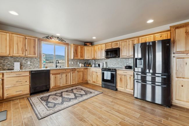 Kitchen featuring range with electric cooktop, black dishwasher, light stone counters, and stainless steel fridge with ice dispenser | Image 27