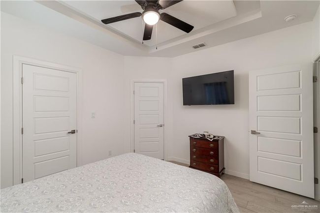Bedroom featuring ceiling fan, visible vents, baseboards, a tray ceiling, and light wood-style flooring | Image 9