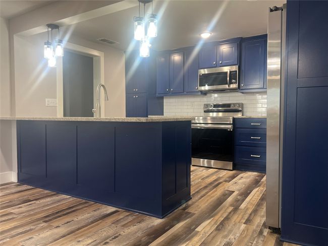 Kitchen with blue cabinets, appliances with stainless steel finishes, dark wood finished floors, tasteful backsplash, and hanging light fixtures | Image 9
