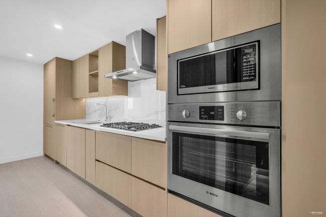 Kitchen with wall chimney exhaust hood, light brown cabinets, modern cabinets, light countertops, and stainless steel appliances | Image 5