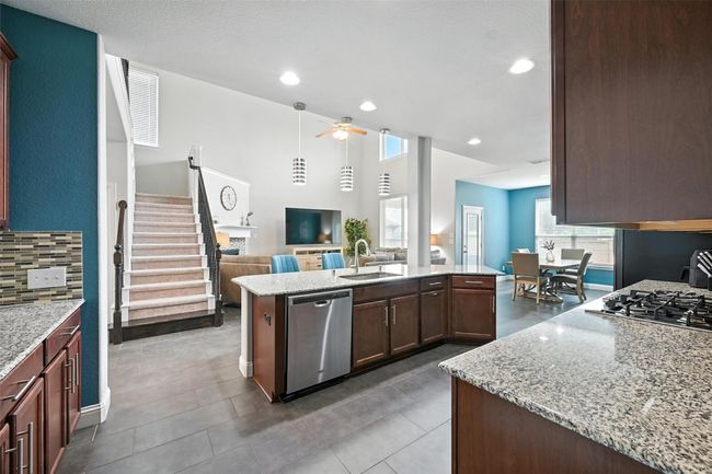 Kitchen with ceiling fan, open floor plan, stainless steel appliances, light stone counters, and a center island with sink | Image 10