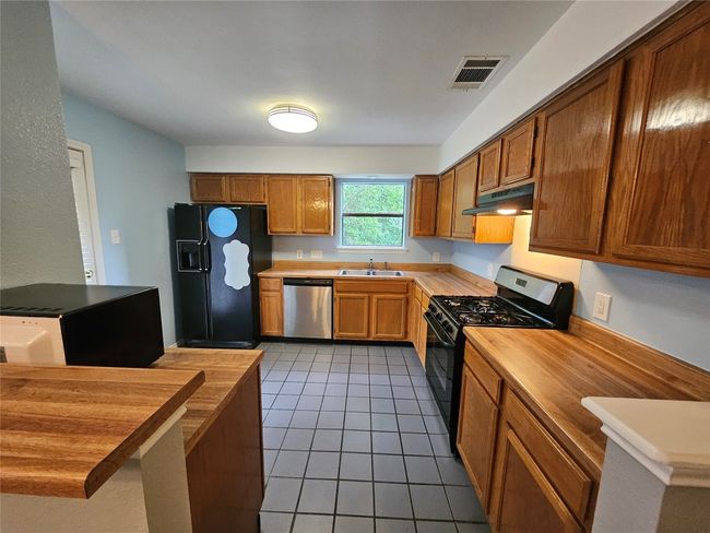 Kitchen with stainless steel dishwasher, butcher block counters, range with gas cooktop, and black refrigerator with ice dispenser | Image 15