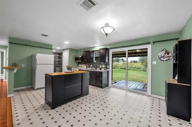 Kitchen with white appliances, wood counters, decorative backsplash, a kitchen island, and light flooring | Image 8