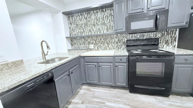 Kitchen with black appliances, gray cabinets, a sink, light wood-style flooring, and light stone counters | Image 6