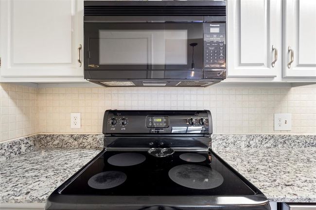Kitchen featuring electric stove, black microwave, white cabinets, decorative backsplash, and light stone countertops | Image 14
