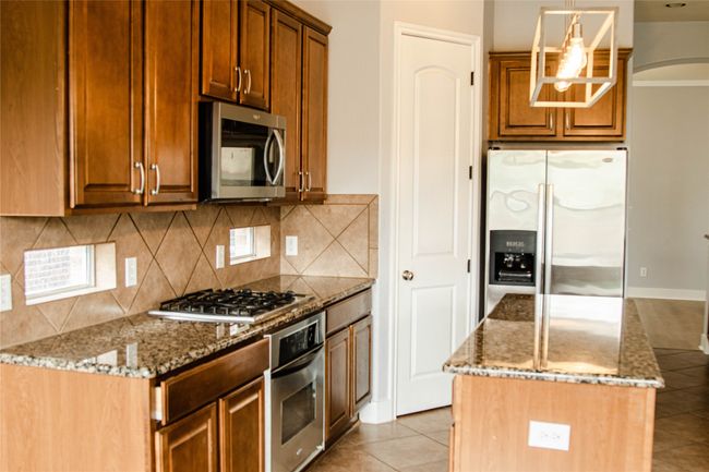 Kitchen with appliances with stainless steel finishes, light stone counters, tasteful backsplash, a center island, and arched walkways | Image 8