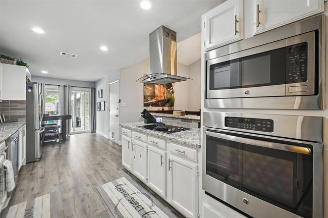 Kitchen featuring stainless steel appliances, island exhaust hood, white cabinetry, light stone counters, and recessed lighting | Image 12