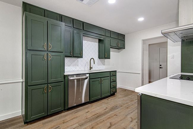 Kitchen with green cabinetry, stainless steel dishwasher, a sink, island exhaust hood, and light wood-style flooring | Image 15