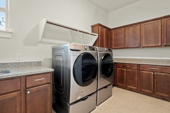 Laundry room featuring cabinet space, washer and dryer, a sink, and light tile patterned floors | Image 31