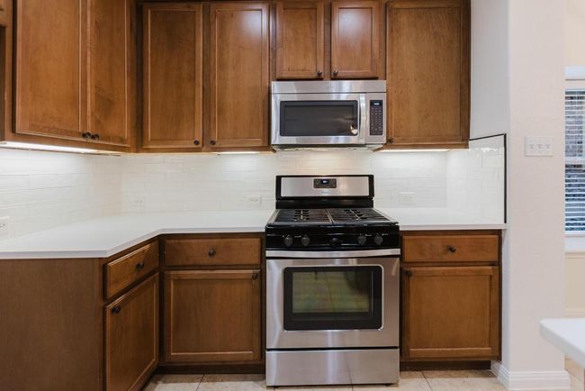 Kitchen featuring tasteful backsplash, baseboards, light countertops, light tile patterned floors, and appliances with stainless steel finishes | Image 13