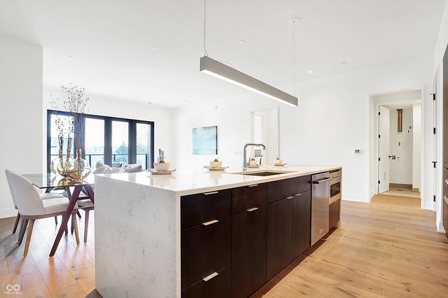 The kitchen has a large center island with walnut drawers and cabinets, dishwasher, drawer microwave and a beautiful quartz waterfall countertop | Image 11