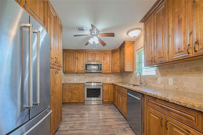 This kitchen features warm wood cabinetry (with tons of storage), stainless steel appliances, and granite countertops. It has a modern feel with a tile backsplash, ceiling fan, and ample natural light from window overlooking backyard | Image 10