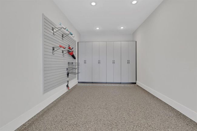 The three-car tandem garage has spacious storage area with sleek cabinets and a slat wall for hanging tools, set against a clean, modern design with a epoxy floor and recessed lighting. Ideal for an organized workspace or garage. | Image 7