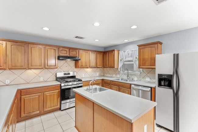 Kitchen featuring under cabinet range hood, stainless steel appliances, visible vents, and a sink | Image 13