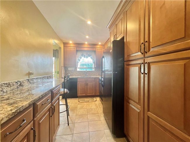Kitchen with light tile patterned flooring, sink, dishwashing machine, black fridge, and light stone counters | Image 9