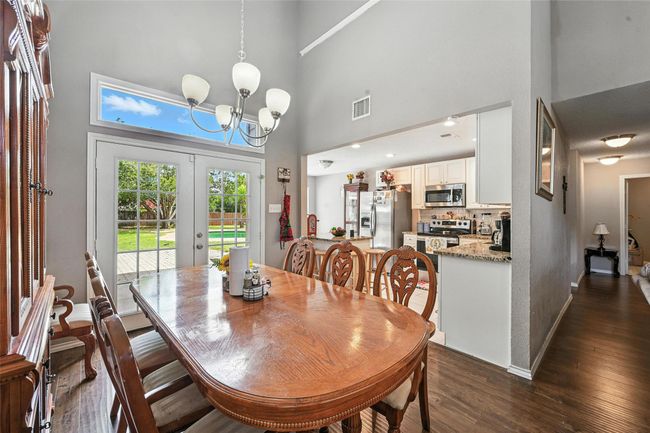 Dining area featuring a high ceiling, dark wood-style flooring, a chandelier, and french doors | Image 13