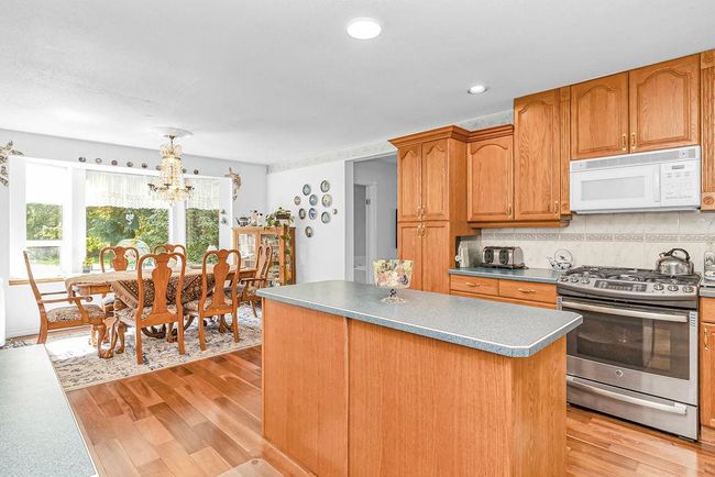 Kitchen with light wood-type flooring, a chandelier, white microwave, a center island, and stainless steel gas range oven | Image 8