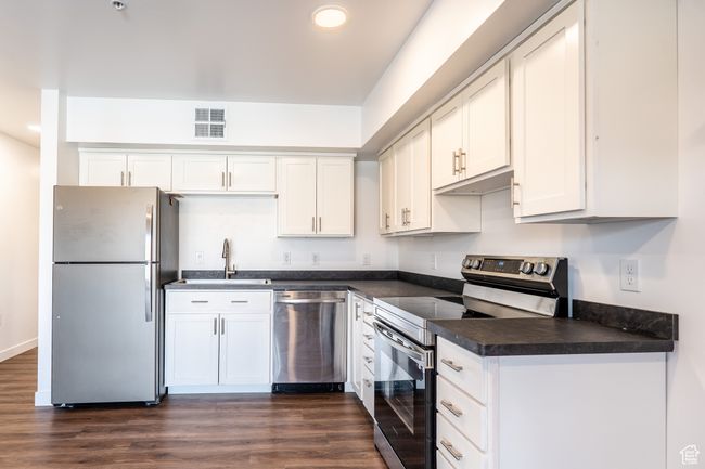 Kitchen featuring visible vents, dark wood-type flooring, a sink, dark countertops, and stainless steel appliances | Image 6