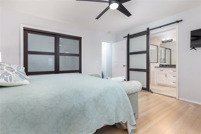 Bedroom with light wood-type flooring, ceiling fan, ensuite bathroom, and a barn door | Image 28