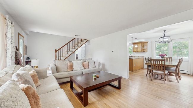 Living room featuring cozy corner gas stove, light wood finished floors, stairway, front entry and baseboard heating. | Image 8