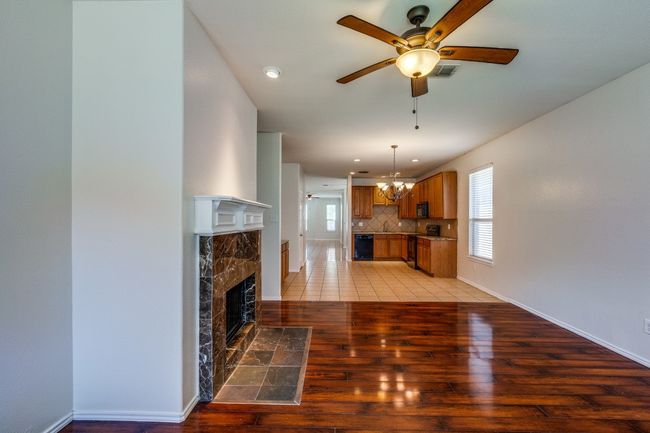 Unfurnished living room featuring visible vents, baseboards, light wood-type flooring, a high end fireplace, and ceiling fan with notable chandelier | Image 6