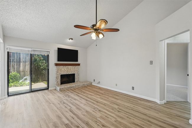 Unfurnished living room featuring lofted ceiling, ceiling fan, LVT floors, and a wood burning fireplace | Image 5