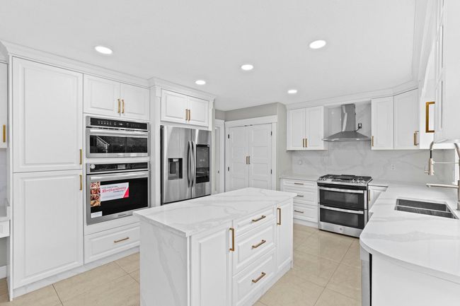 Kitchen featuring a center island, a sink, wall chimney range hood, white cabinetry, and stainless steel appliances | Image 9